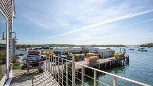 A waterfront dock with a barbecue grill, storage containers, and a building with a flat roof.
