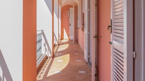 Un couloir aux plafonds voûtés et au sol carrelé, qui mène à des portes équipées de volets.