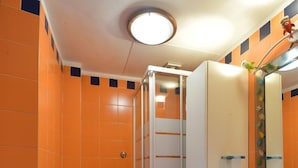 A bathroom with orange tiles, a white sink, a glass shower enclosure, and a toilet with a green seat. - Accogliente Appartamento (Roma)