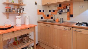 A kitchen with wooden cabinets, a sink, and a stove. There are shelves with jars and a kettle. - Accogliente Appartamento (Roma)