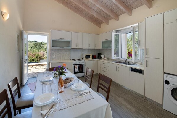 Una cocina moderna con armarios blancos, una mesa de comedor para cuatro personas y vistas al exterior.