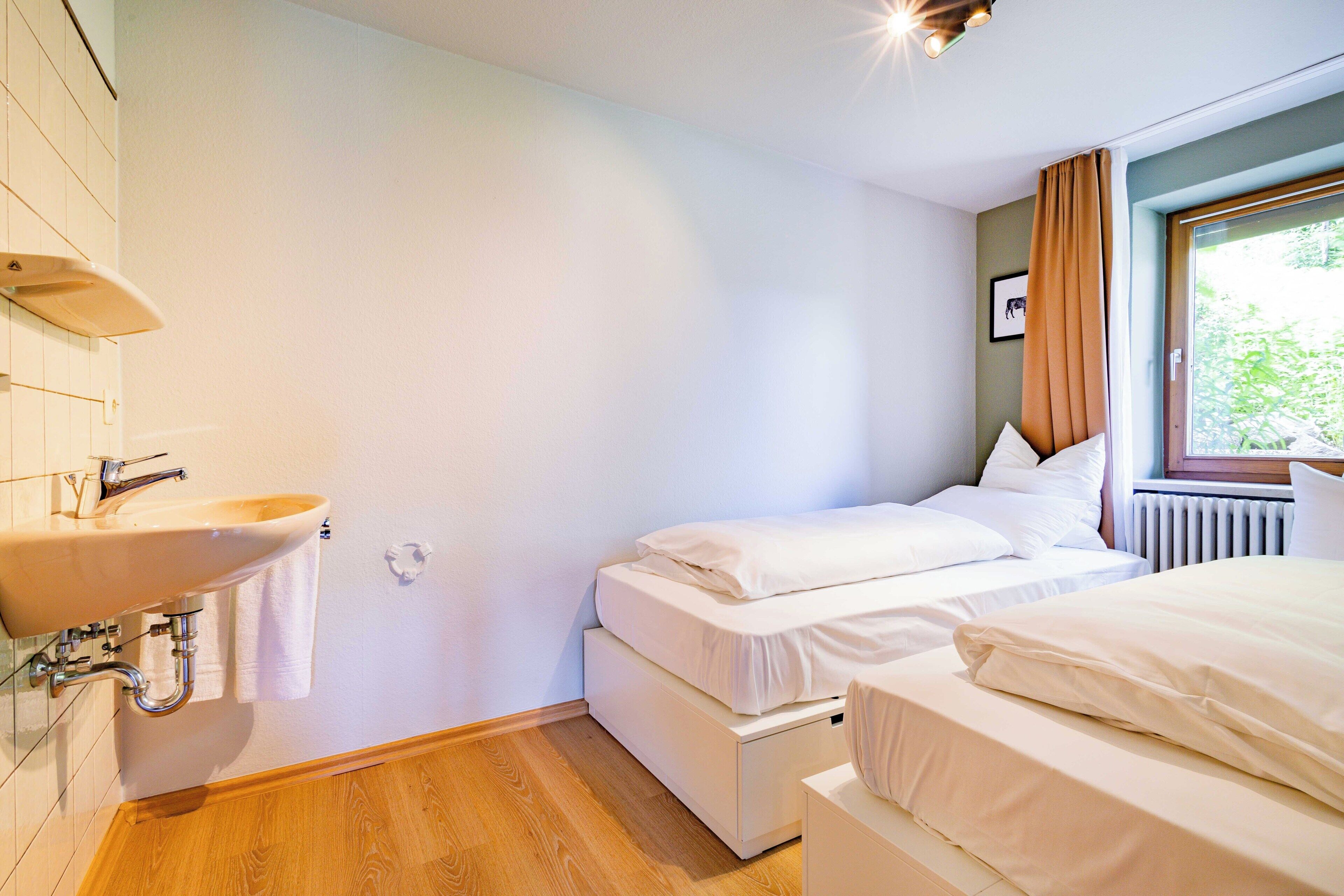Ein Hotelzimmer mit Holzboden, einem weißen Waschbecken und einem Fenster mit Vorhängen.