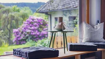 Une pièce chaleureuse avec une table en bois, une chaise, une petite table sur laquelle est posée une bougie, et une vue sur une maison et un jardin.