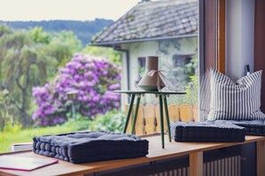 Una habitación acogedora con una mesa de madera, una silla, una mesita con una vela y vistas a una casa y un jardín.