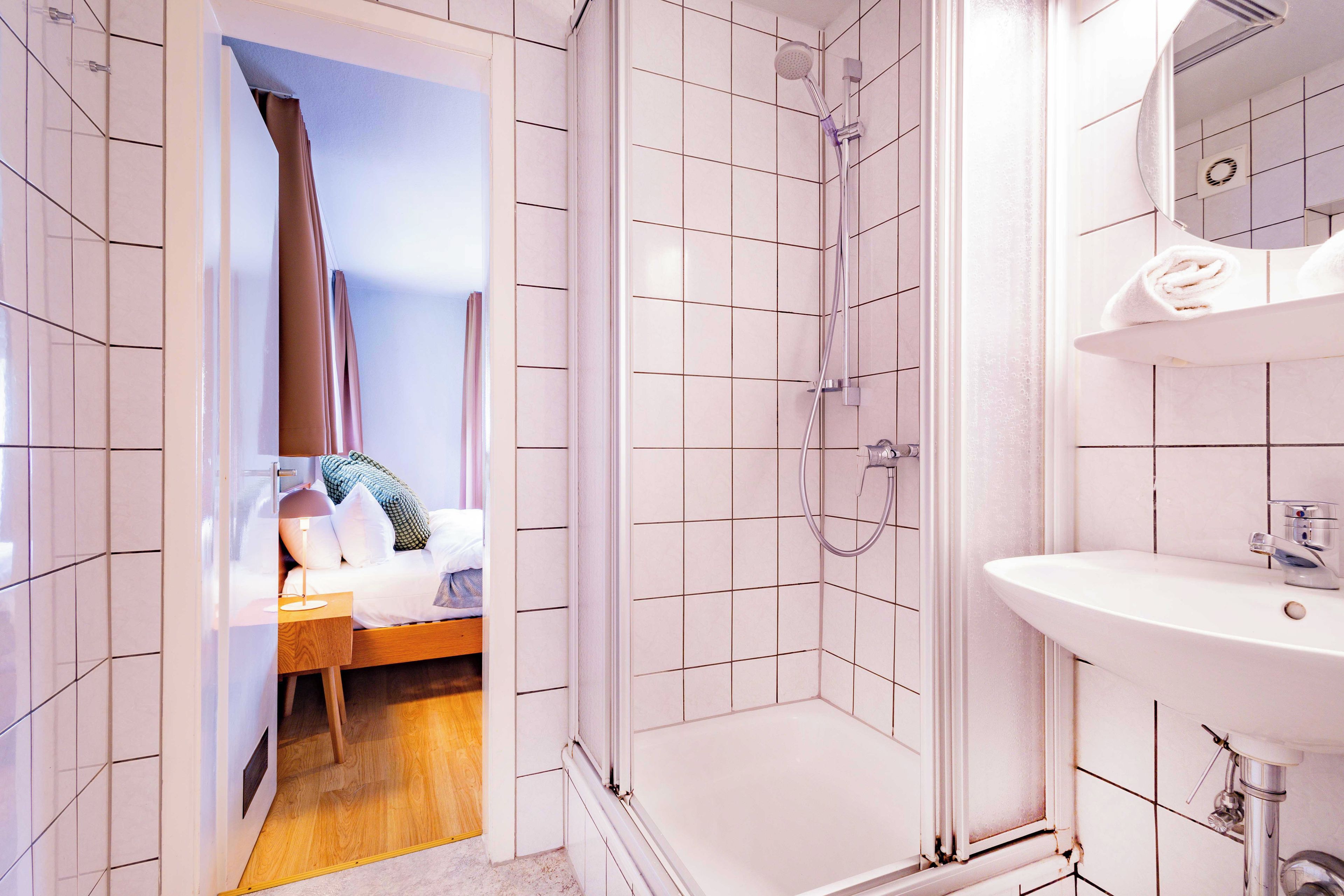 Une salle de bain d’hôtel équipée d’une douche, d’un lavabo et d’un lit avec une tête de lit en bois.