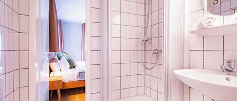 Une salle de bain d’hôtel équipée d’une douche, d’un lavabo et d’un lit avec une tête de lit en bois.