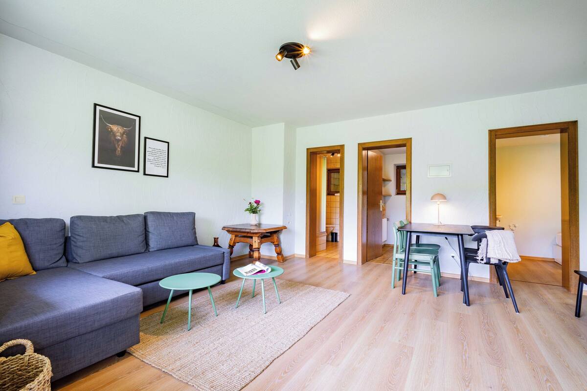 A living room with a grey sofa, a small round table, and a dining area with a table and chairs.