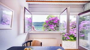 A room with a table, a chair, and a window with an open door. - Titisee Haus an der Sonne by Kuckucksnester (Hinterzarten)
