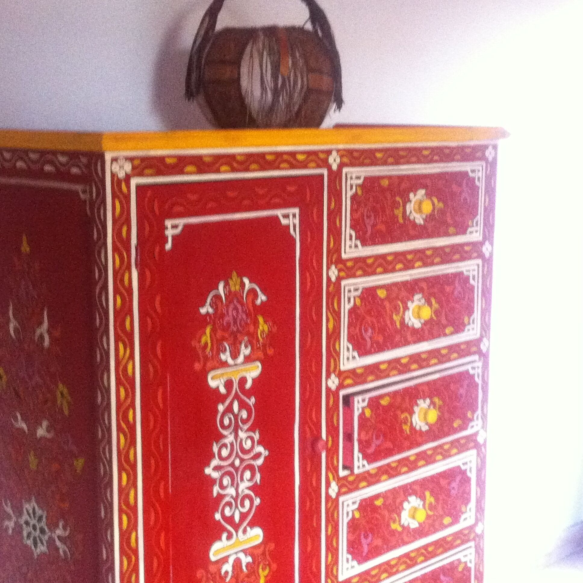 A red cabinet with ornate white patterns and a handle on top.