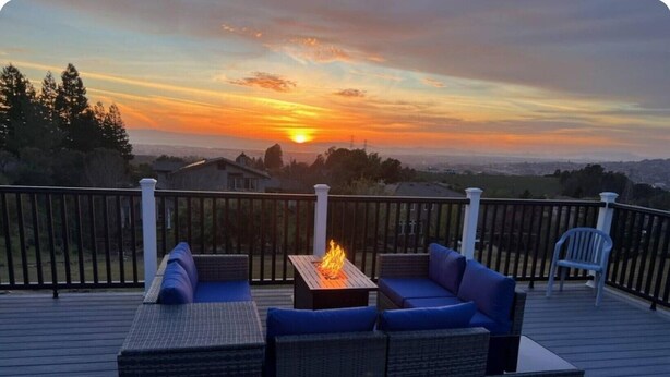 Terraza con mobiliario exterior y una fogata, con vista a un hermoso atardecer.