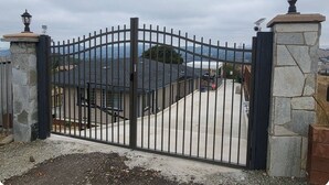 Una entrada protegida por un portón metálico, pilares de piedra y una farola.