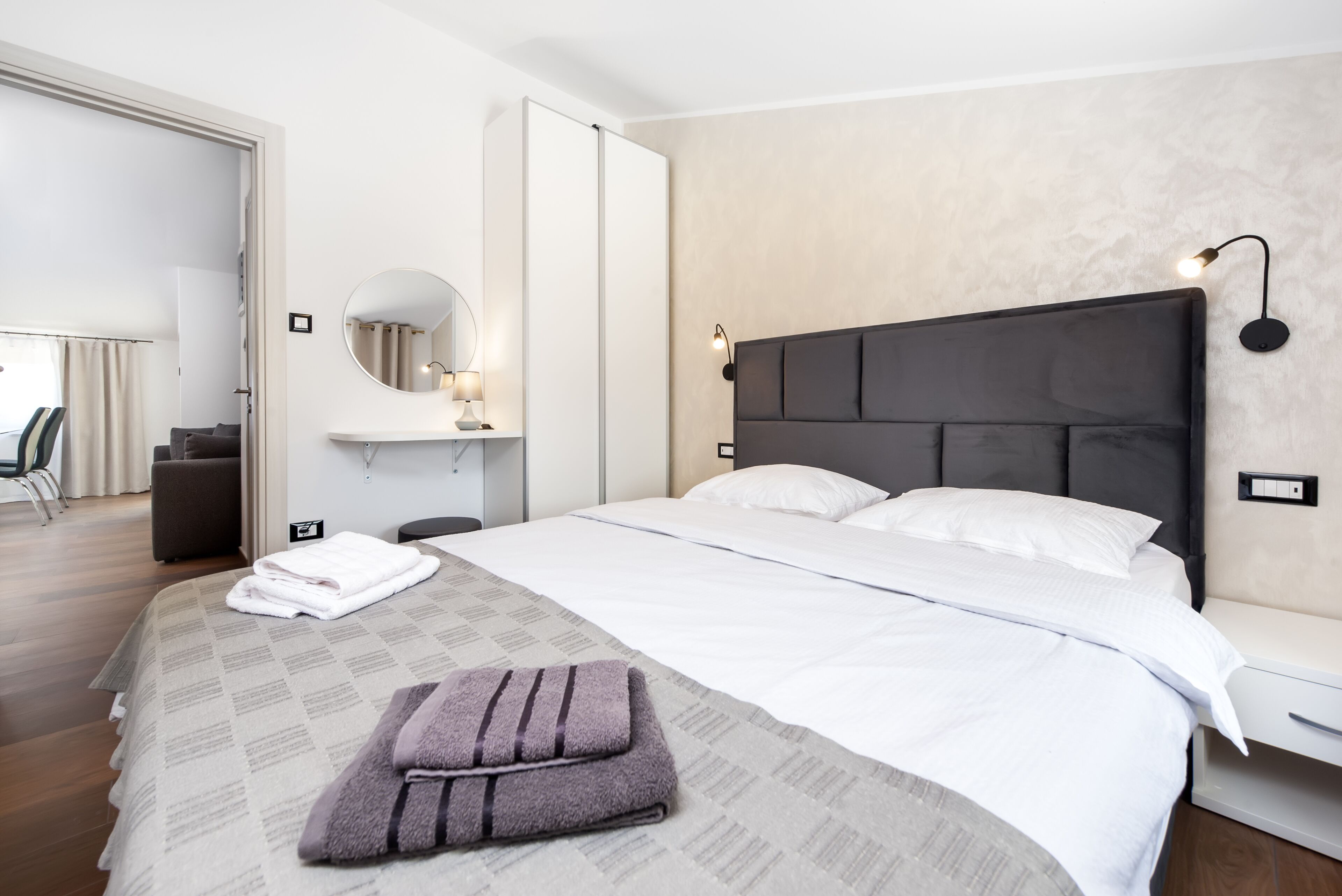Una habitación de hotel con una cama grande, una mesita de noche, un espejo y una lámpara fijada a la pared.
