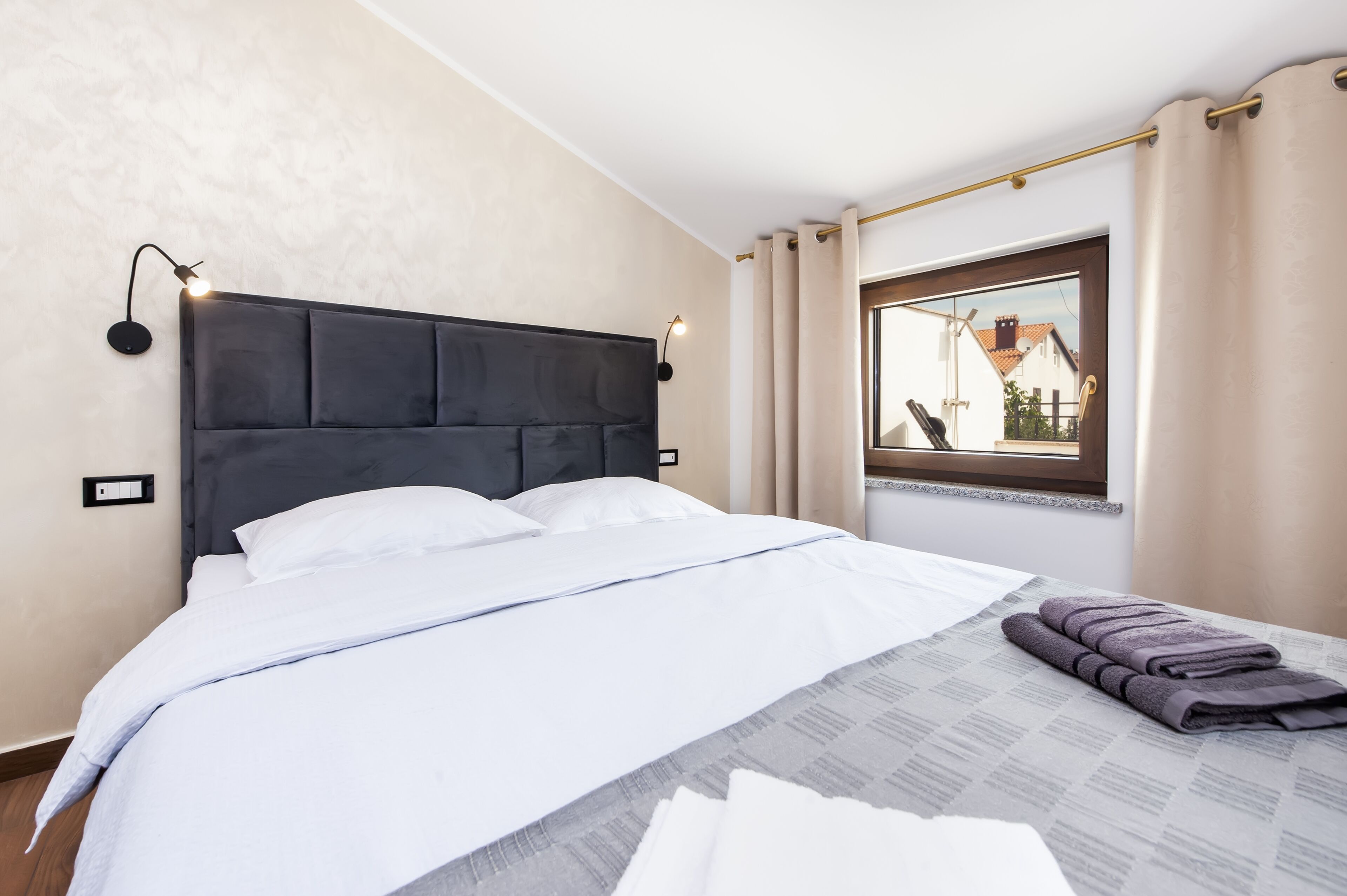 Un lit bien fait, avec du linge de lit blanc, une tête de lit sombre et une fenêtre avec des rideaux.