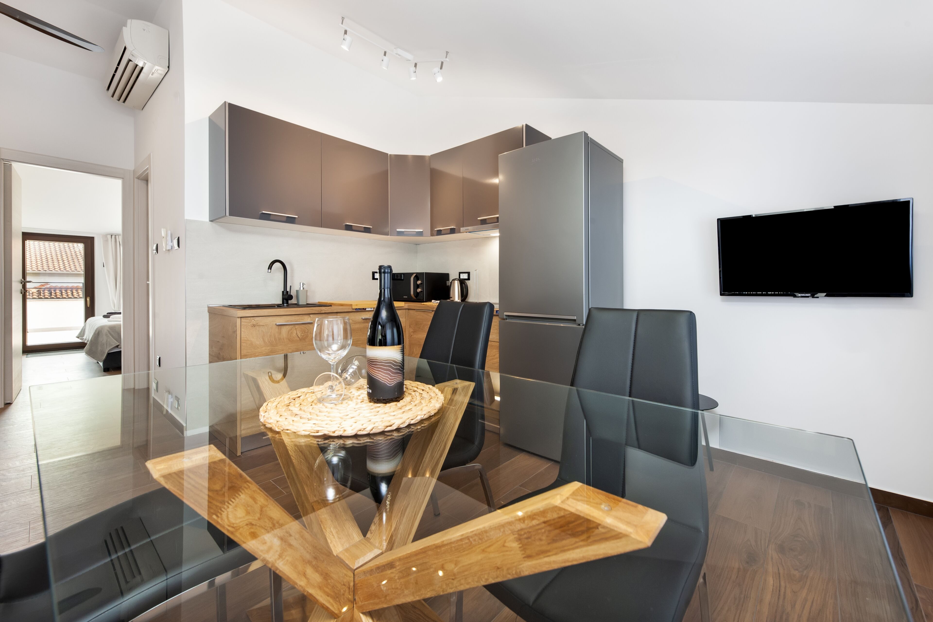 A modern kitchen with a built-in oven, a refrigerator, and a flat-screen TV mounted on the wall.