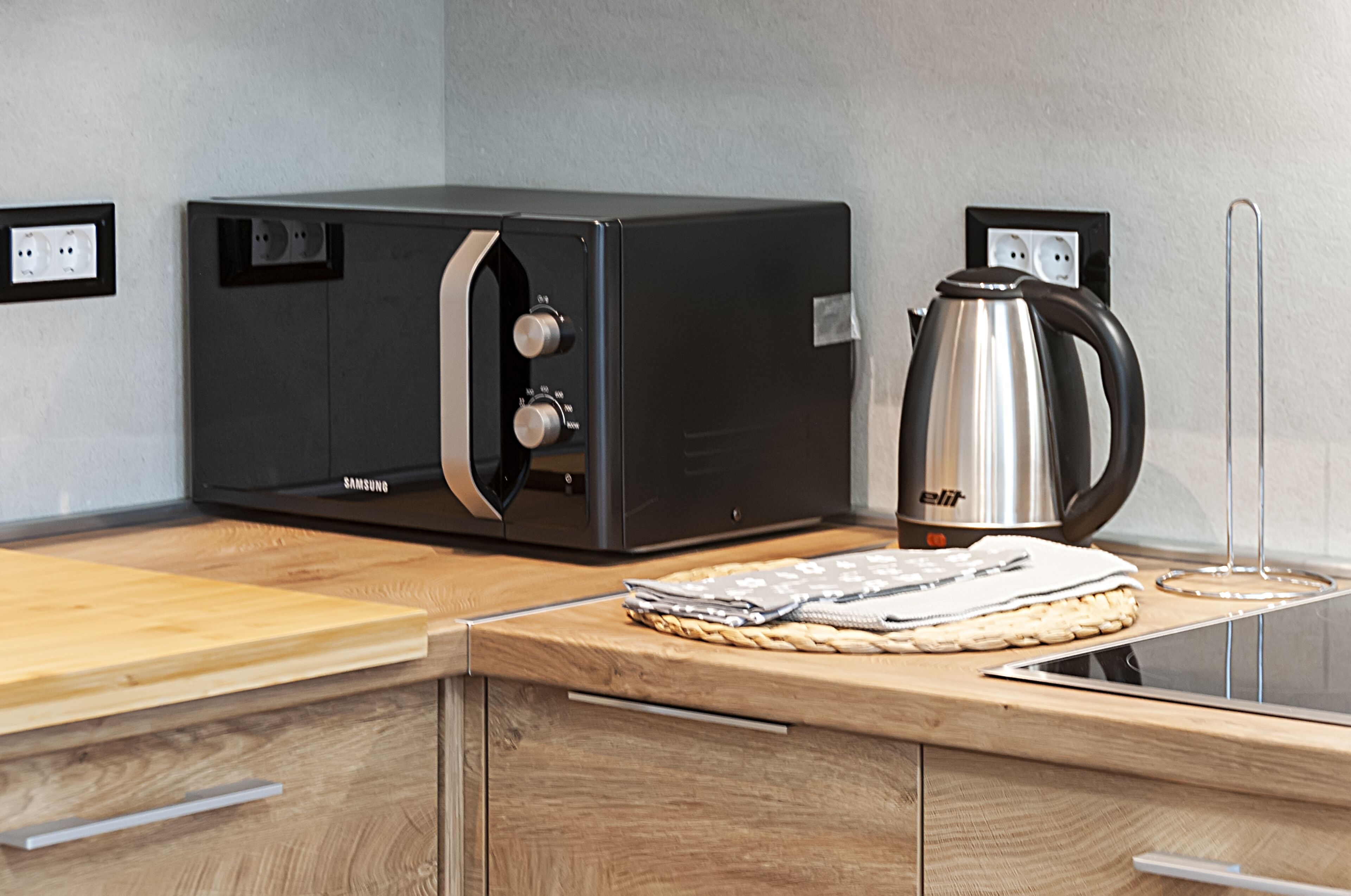 A kitchen with a Samsung microwave, a kettle, and a wooden countertop.