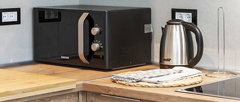 A kitchen with a Samsung microwave, a kettle, and a wooden countertop.