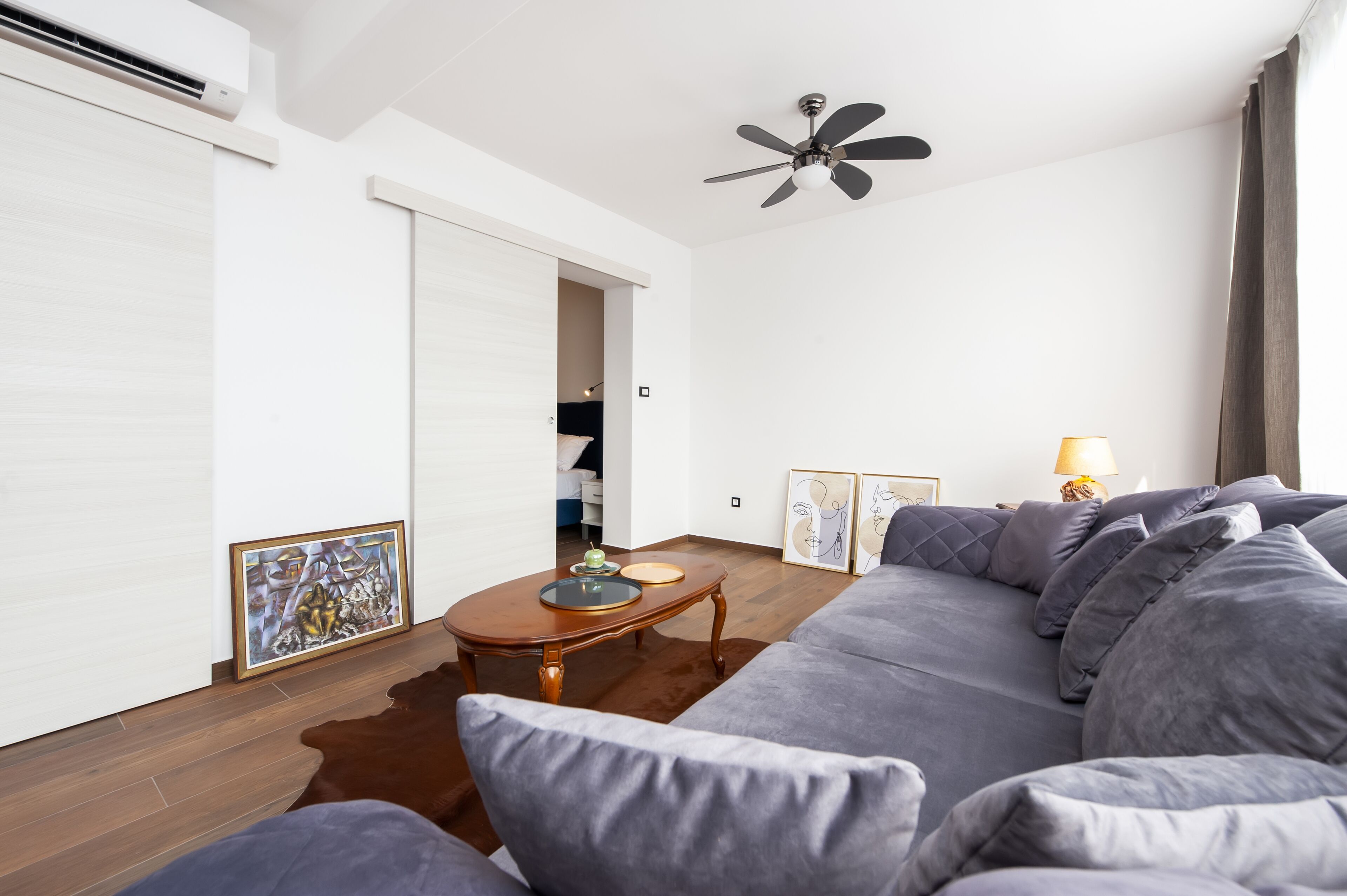 Un salon moderne avec un canapé gris, une table basse en bois et un ventilateur de plafond.