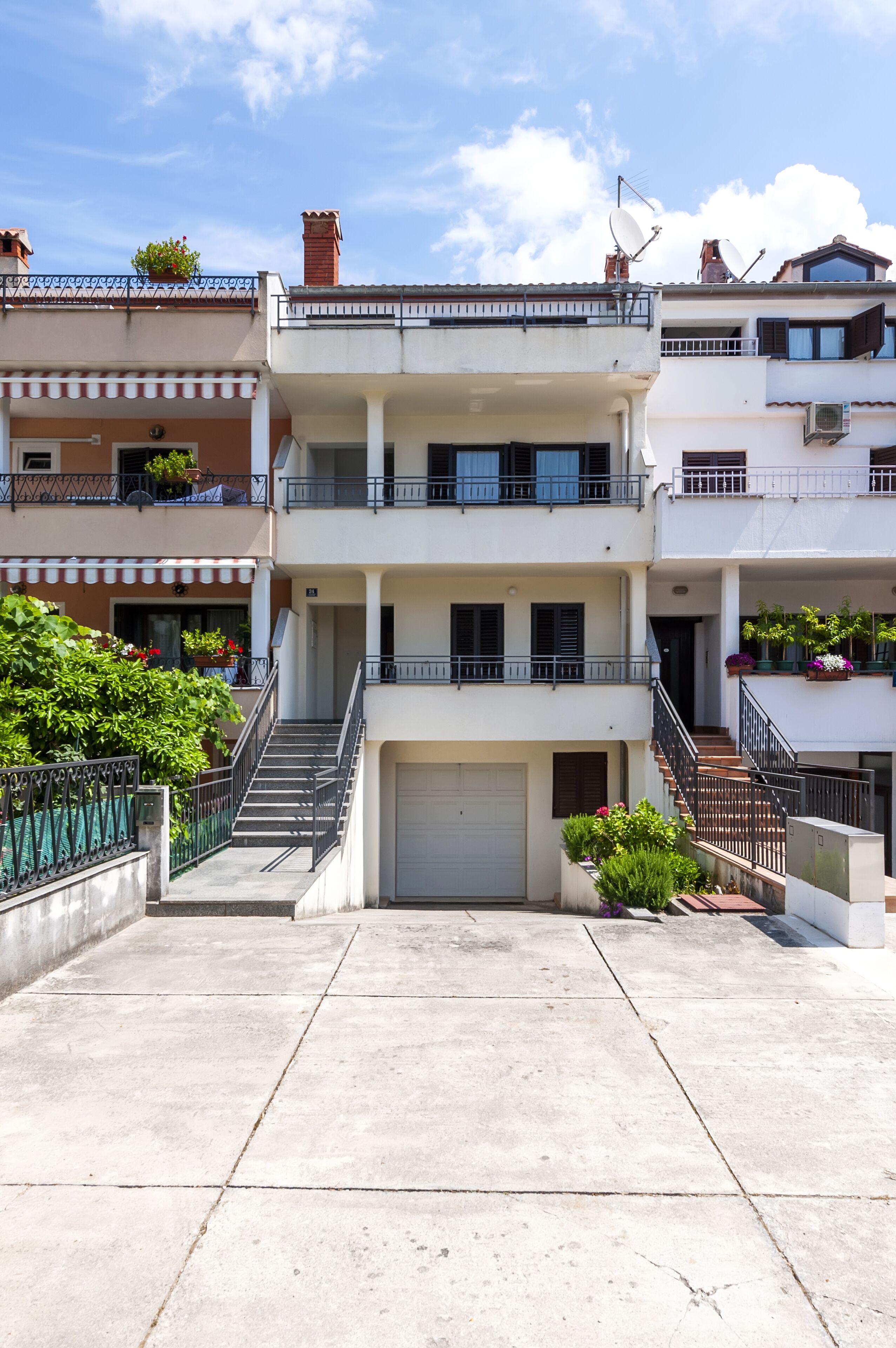 A multi-story residential building with a central staircase, balconies, and potted plants.