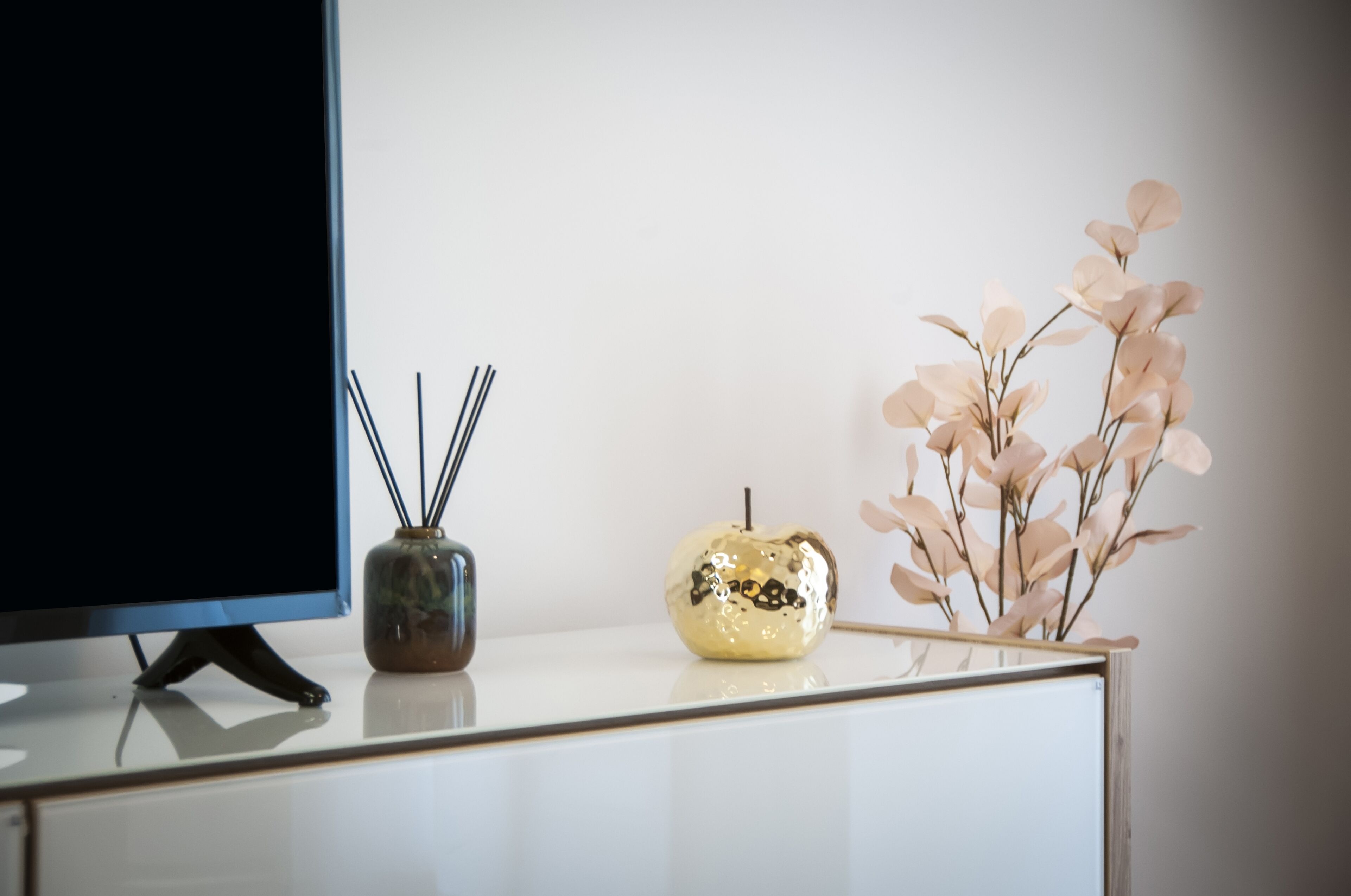 A modern, minimalist desk with a flat-screen TV, a decorative vase, and a small plant.