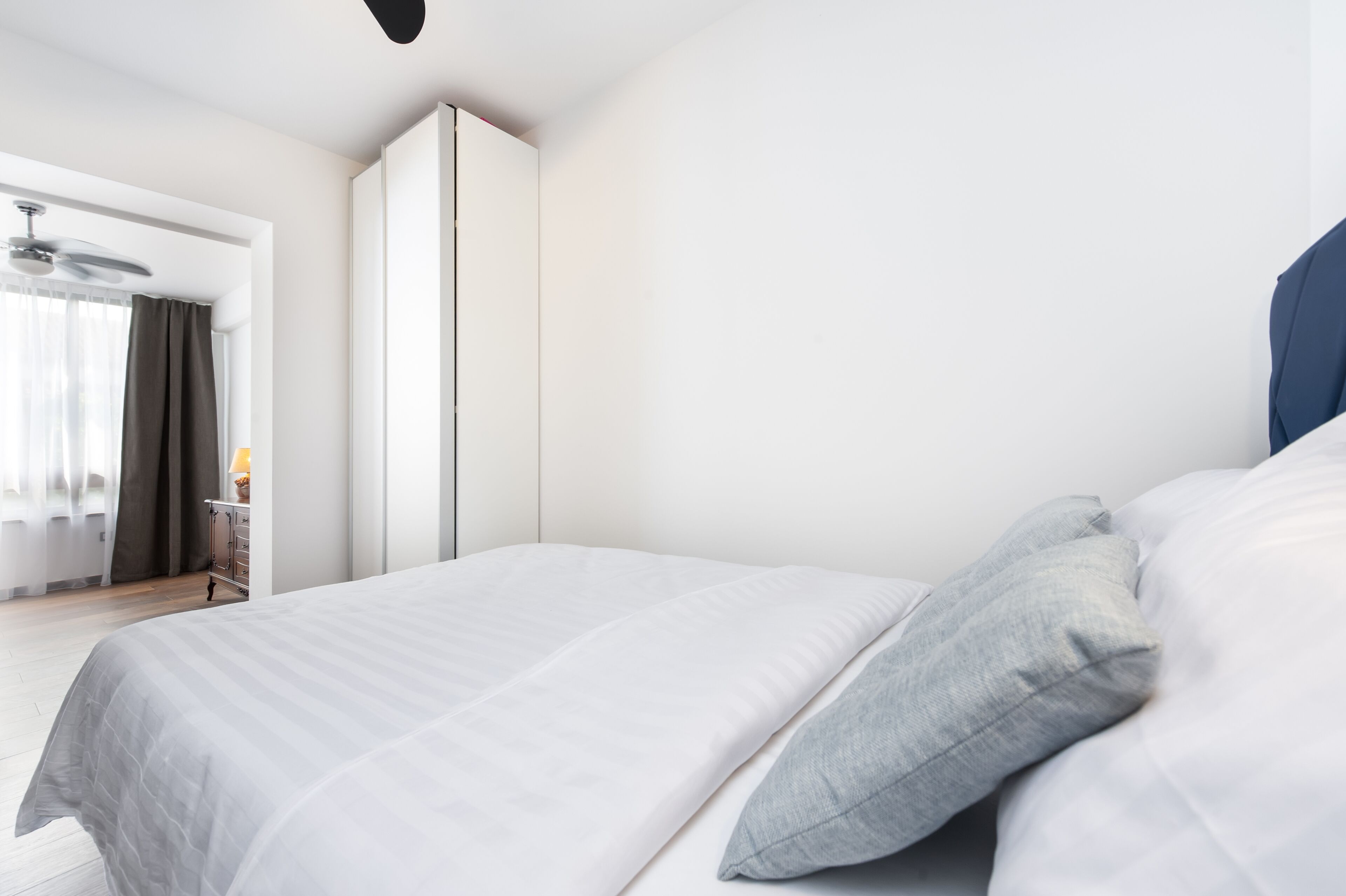 A modern bedroom with a large bed, a wardrobe, and a desk with a lamp.