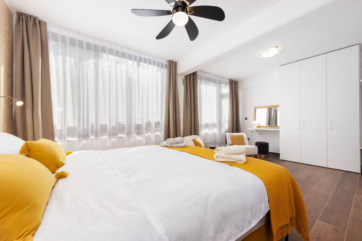 A hotel room with a large bed, a ceiling fan, a wardrobe, and a desk with a mirror.
