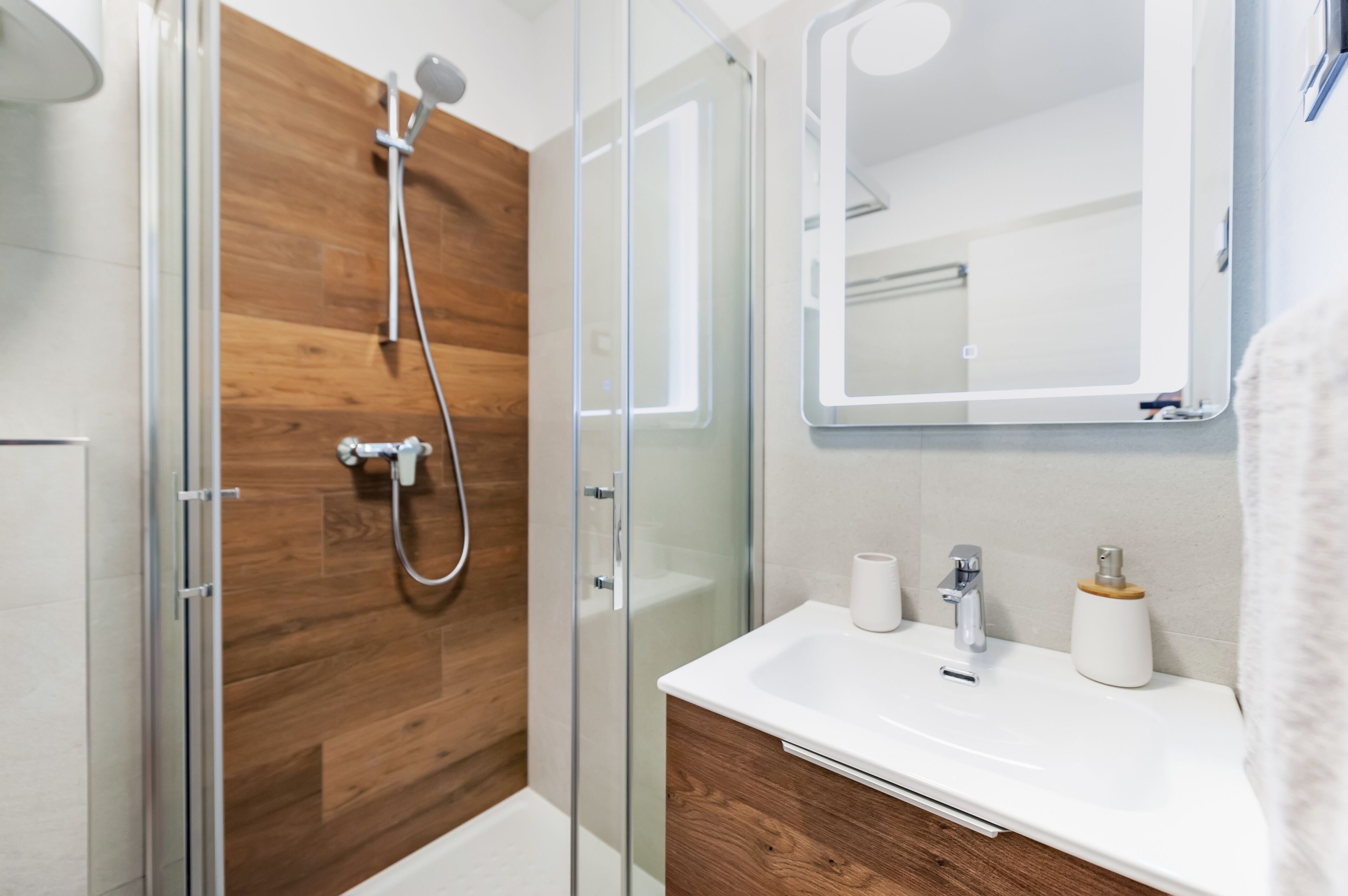 Un baño moderno con cabina de ducha de vidrio, tocador de madera y un espejo grande.