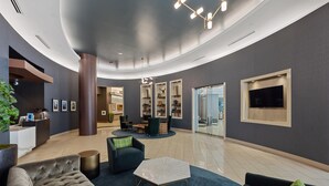 Eine moderne Lobby mit gewölbter Decke, Sitzbereichen, einem Empfangstresen und einem wandmontierten Fernseher.