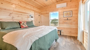 A wooden-paneled bedroom with a bed, pillows, a ceiling fan, a window, and a wall-mounted air conditioner. - Peaceful quite cabin to kick back, relax and recharge! (Robert Lee)