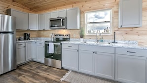A modern kitchen with white cabinets, stainless steel appliances, and a wooden ceiling. - Peaceful quite cabin to kick back, relax and recharge! (Robert Lee)