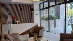 A modern lobby with a sofa, a coffee table, and a large glass door leading outside. - EÓN 6 - Estudio Moderno, Vista Volcán, Aire Acondicionado (Ciudad de Guatemala)