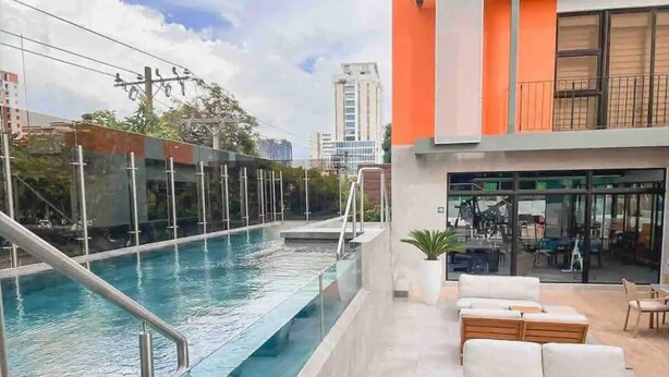 A rooftop pool area with a glass barrier, outdoor seating, and a view of the cityscape. - EÓN 6 - Estudio Moderno, Vista Volcán, Aire Acondicionado (Ciudad de Guatemala)
