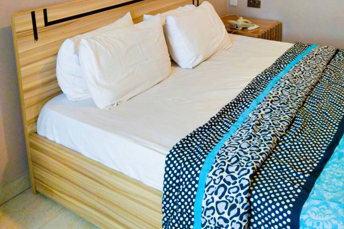 A bed with white bedding, a patterned blanket, and three framed artworks on the wall above.