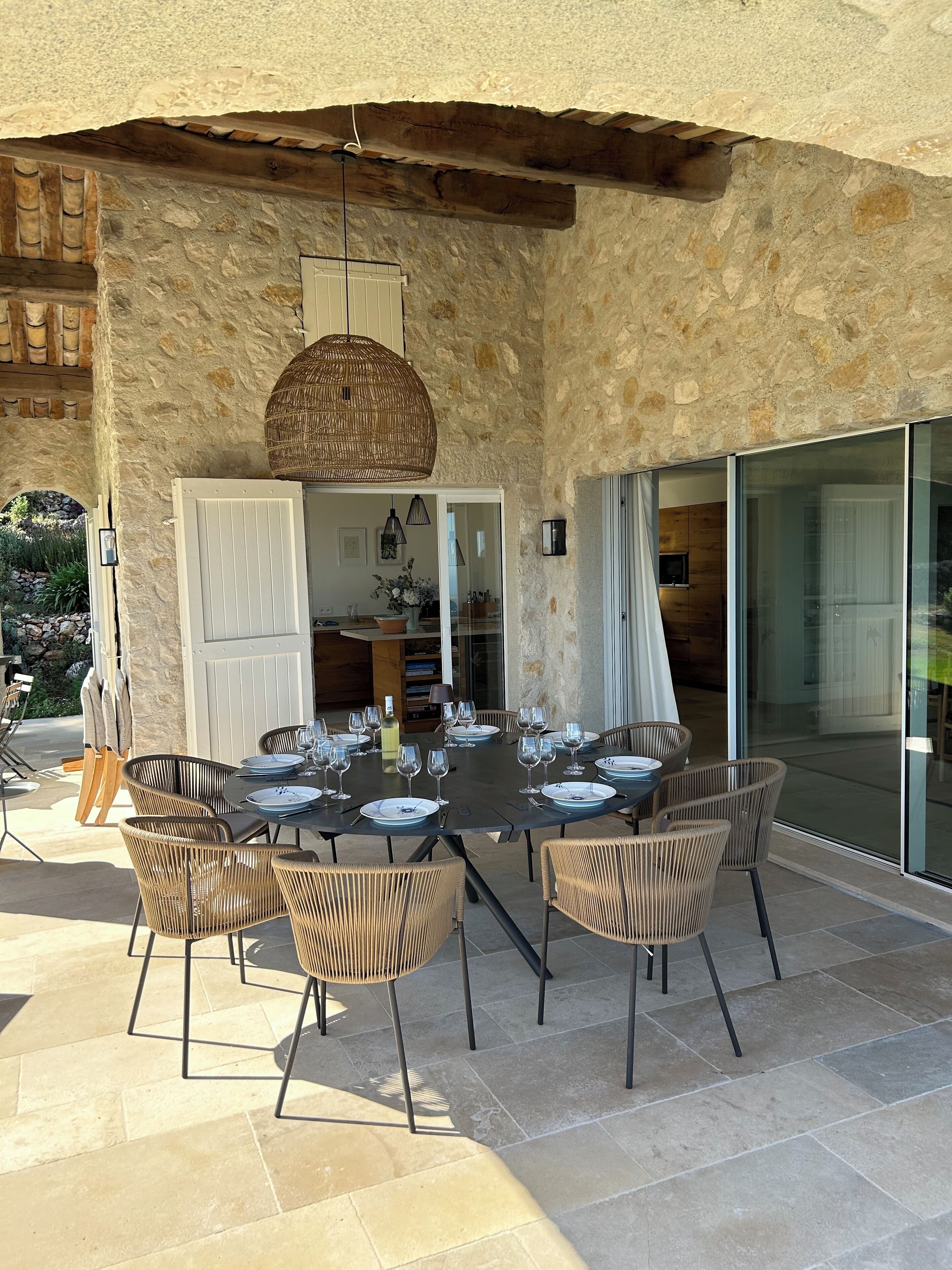 A stone exterior wall with a dining area featuring wicker chairs and a table set for a meal.