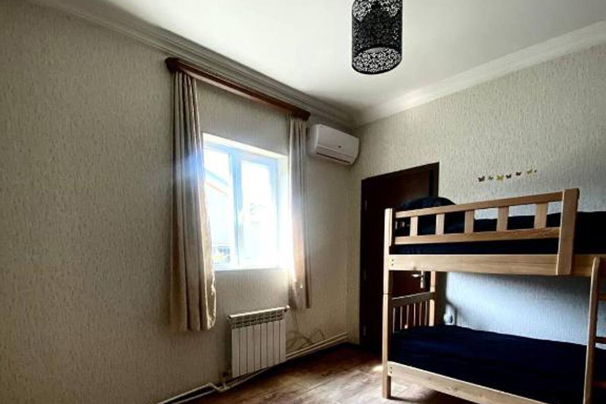A room with a bunk bed, a radiator, a window with curtains, and an air conditioning unit.