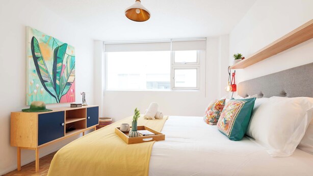 Une chambre à coucher avec un lit, une table de chevet, une fenêtre et un tableau accroché au mur.