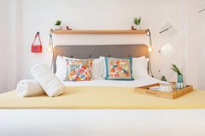 Een netjes opgemaakt bed met bloemenkussens, een nachtkastje met dienblad en wandlampen.