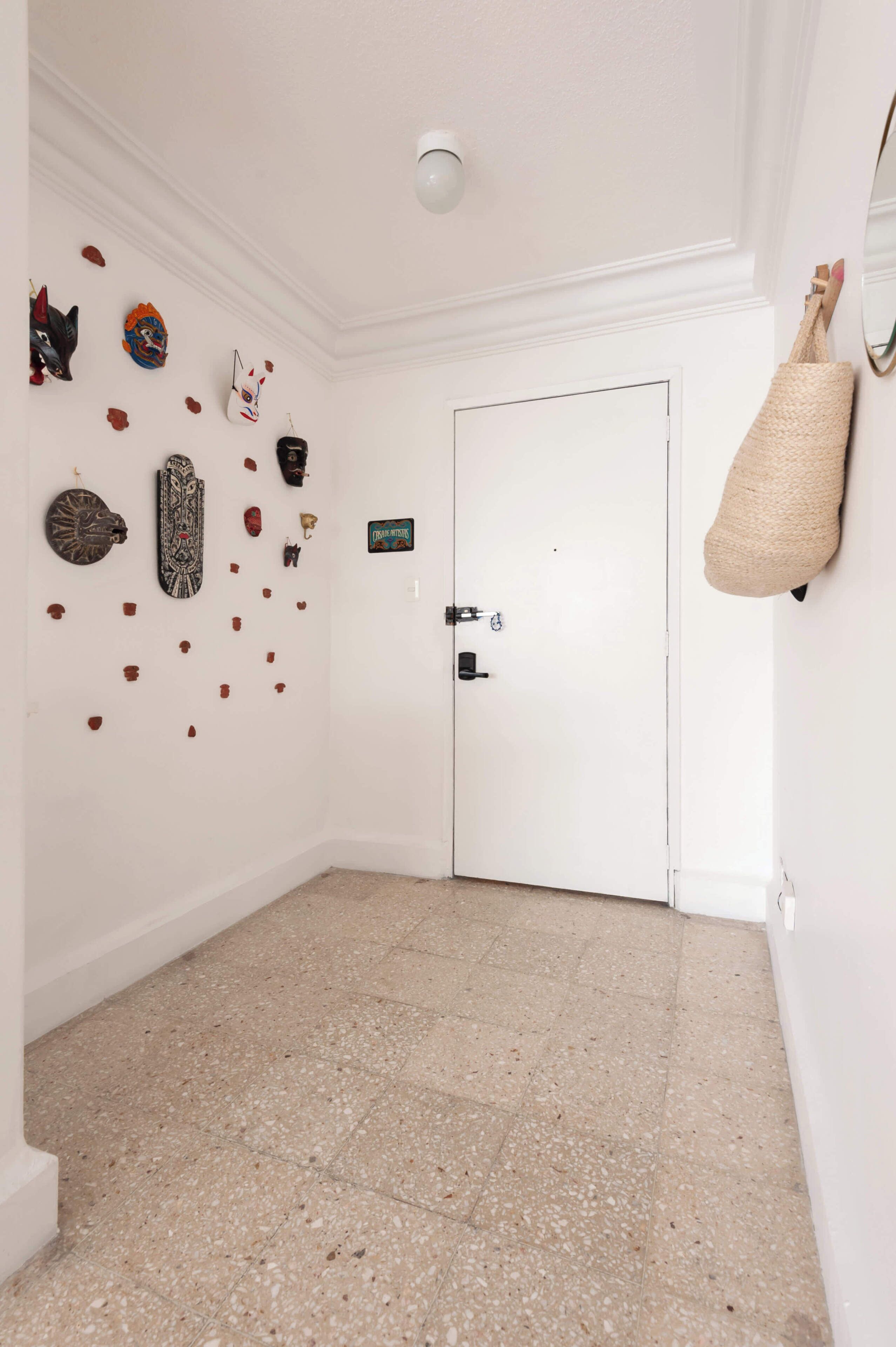 Un pasillo con una puerta blanca, un perchero de pared y varios objetos decorativos.