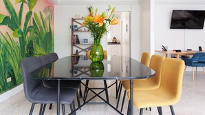 A dining area with a glass table surrounded by chairs, a bookshelf, and a TV mounted on the wall.