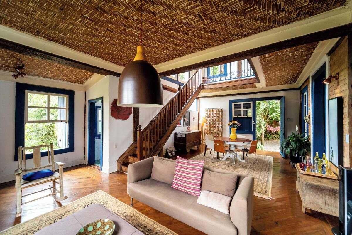 Un vaste espace de vie doté d’un plafond en bois, d’un canapé avec des coussins, d’une table à manger avec des chaises et d’un escalier menant à un niveau supérieur.