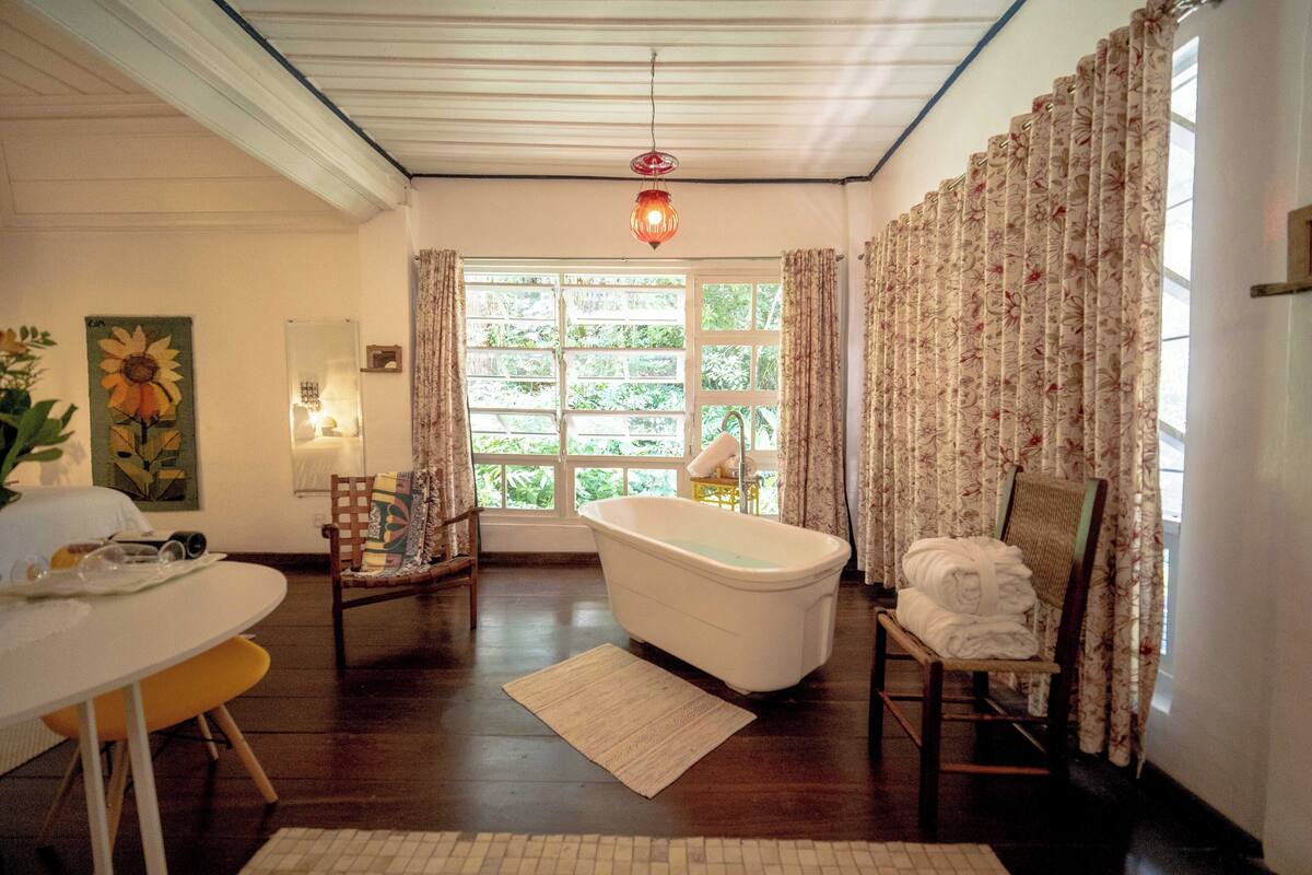 Une pièce avec une baignoire, une table à manger avec des chaises, un tapis et une fenêtre avec des rideaux.