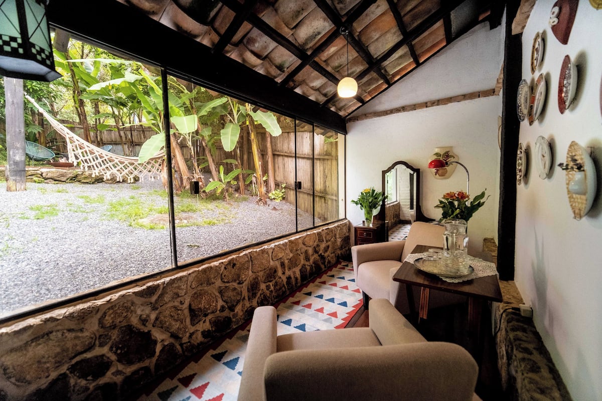 Une pièce chaleureuse avec un mur en pierre, un hamac à l’extérieur et un coin repas avec une table et des chaises.