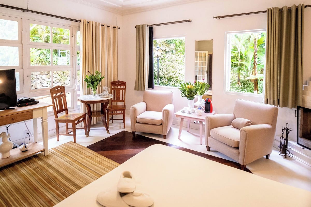 Une chambre d’hôtel comprenant un lit, deux fauteuils, une petite table, un bureau avec un ordinateur et un ventilateur de plafond.
