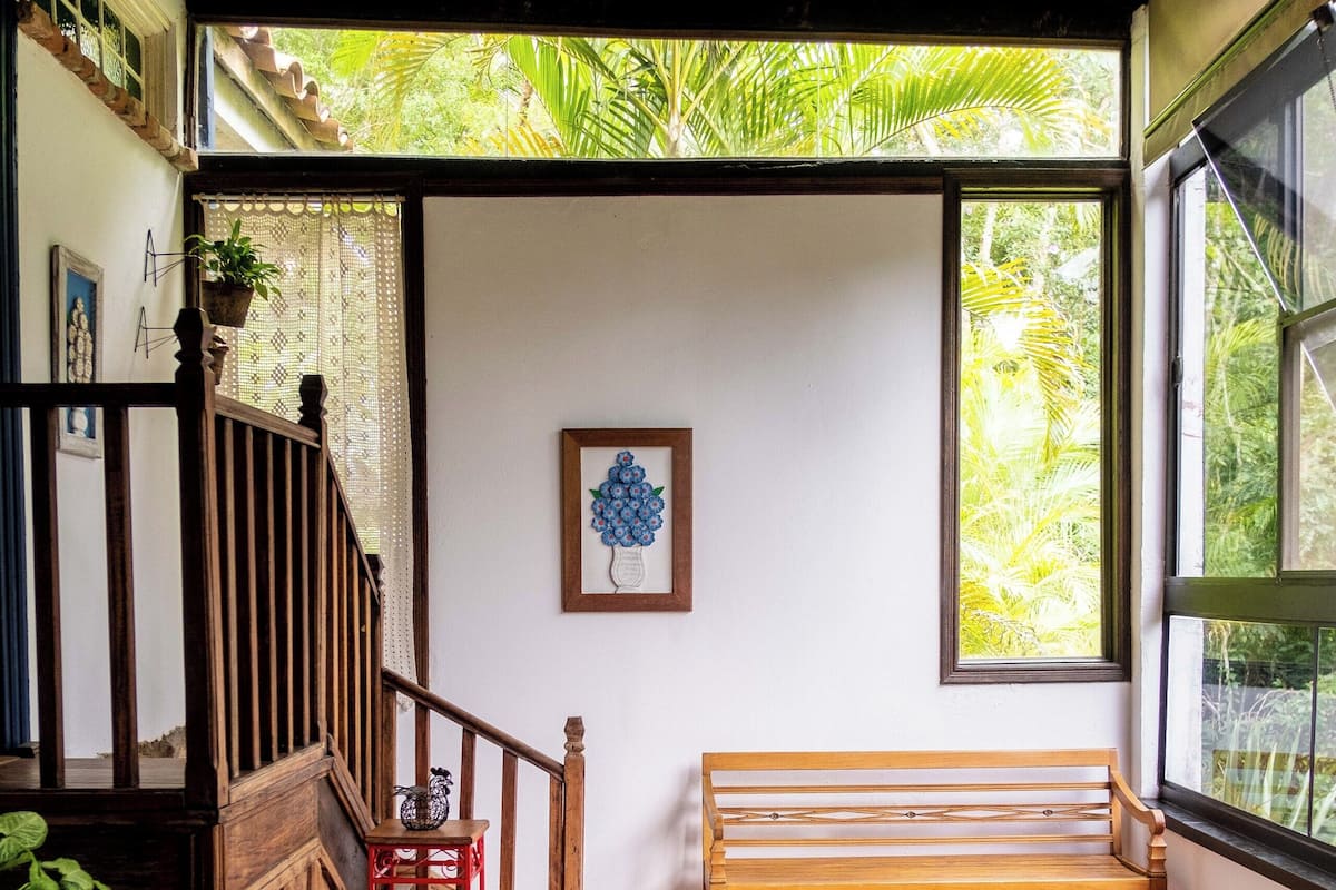 Une pièce comprenant un lit, un banc en bois, un escalier et une fenêtre donnant sur un paysage verdoyant.