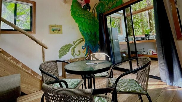 Een kamer met een houten trap, rieten meubels en een muurschildering van twee groene papegaaien.