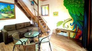 Een kamer met een houten trap, een groene bank, een ronde tafel met stoelen en een kleurrijke papegaaien muurschildering.