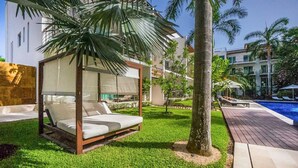 A modern outdoor seating area with a canopy, a pool, and a well-maintained lawn. - Via 38 A13 - Modern Condo - At Via 38 (Playa del Carmen)