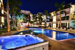 A swimming pool surrounded by palm trees and lounge chairs, with a hot tub in the foreground. - Via 38 A13 - Modern Condo - At Via 38 (Playa del Carmen)