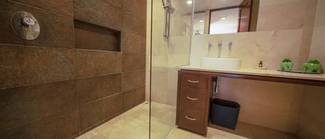 A modern bathroom with a glass shower enclosure, a marble-tiled wall, a wooden vanity with a sink, and a mirror above the vanity.