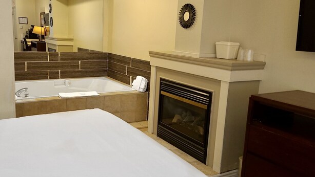 A hotel room with a large bed, a bathtub, a fireplace, and a mirror. - Riviera Inn and Suites 1000 Islands (Gananoque)