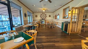 A restaurant with wooden tables and chairs, a large ship's wheel on the wall, and a fireplace. - Riviera Inn and Suites 1000 Islands (Gananoque)